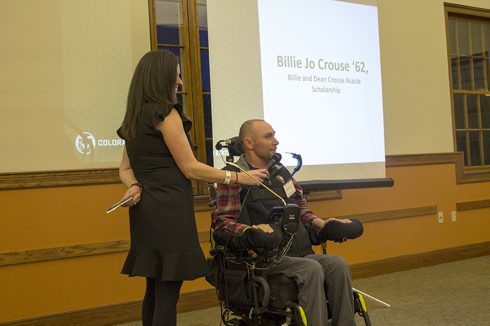 A man in a wheelchair talks into a microphone that a woman holds for him.